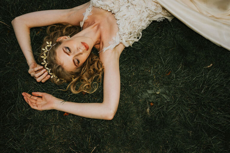 model lies on the grass whilst wearing a designer wedding gown, her eyes are closed and it seems wistful. This images illustrates an article on what to do when a wedding photography business is failing.