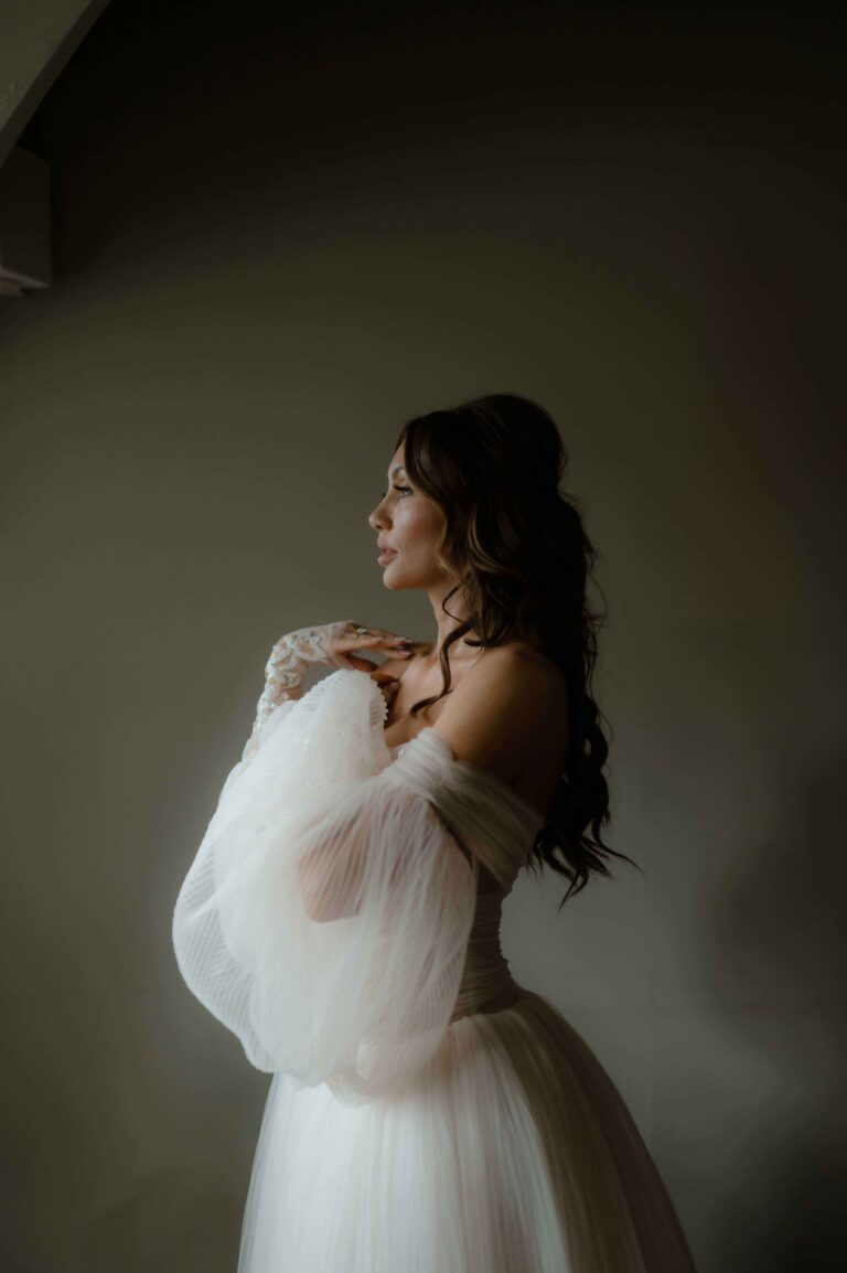 This image shows simplicity in a bridal portrait with a serene bride looking int the light and holding up her hands to show the volumous sleeves of her wedding gown