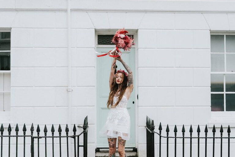 The bride strikes a playful pose with her bouquet outside a classic townhouse, showcasing personality-driven marketing in wedding photography.