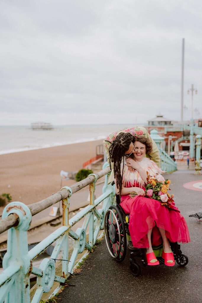 Meg and Xander embracing on Brighton seafront during the Thrive photography conference shoot led by Kim Williams, with the West Pier in the background.