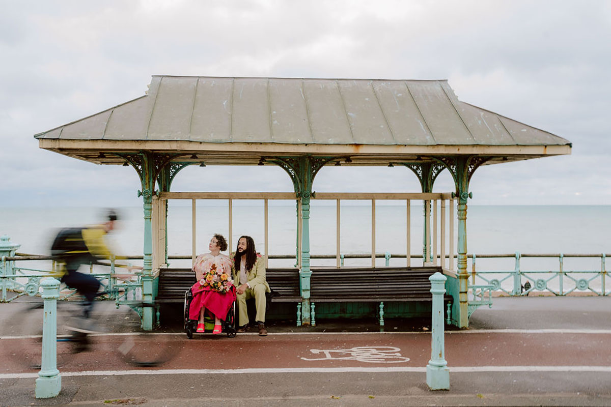 Interabled couple Meg and Xander seated together in a vintage seafront shelter along Brighton promenade during Kim Williams’ Thrive workshop session.