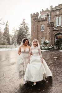 Snowy Wedding Photo at a castle in Scotland with two brides in long wedding dresses by Emma Lawson
